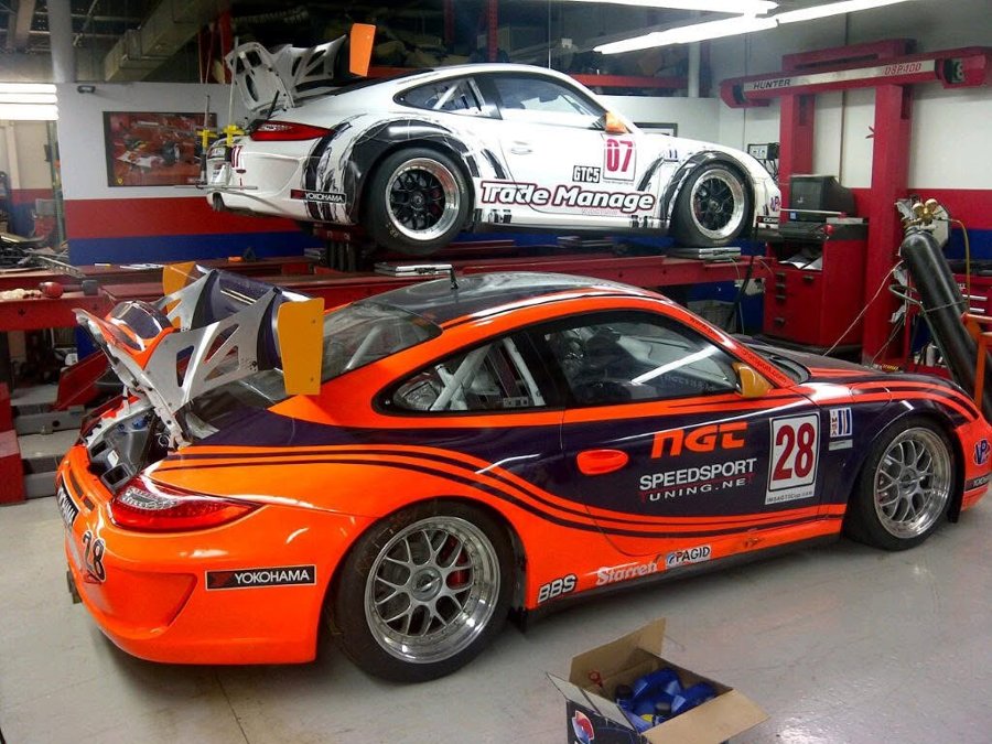 Two Porsche 911 cup cars in the shop, one on the ground and one on the lift above it