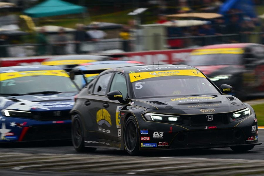 Black Honda Civic FL5 TCR at speed leading another Civic in front of a packed grandstand