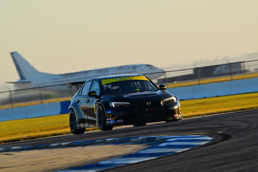 Black Honda Civic TCR on track at dusk with an airliner beyond the fence