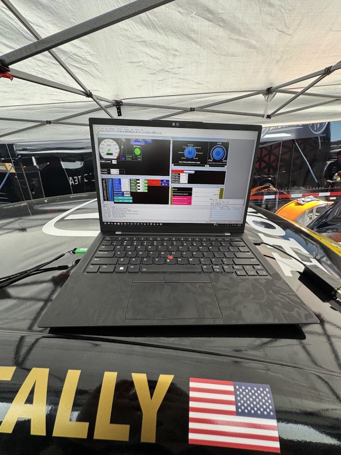 Laptop running data software on the bodywork of a race car under a paddock tent