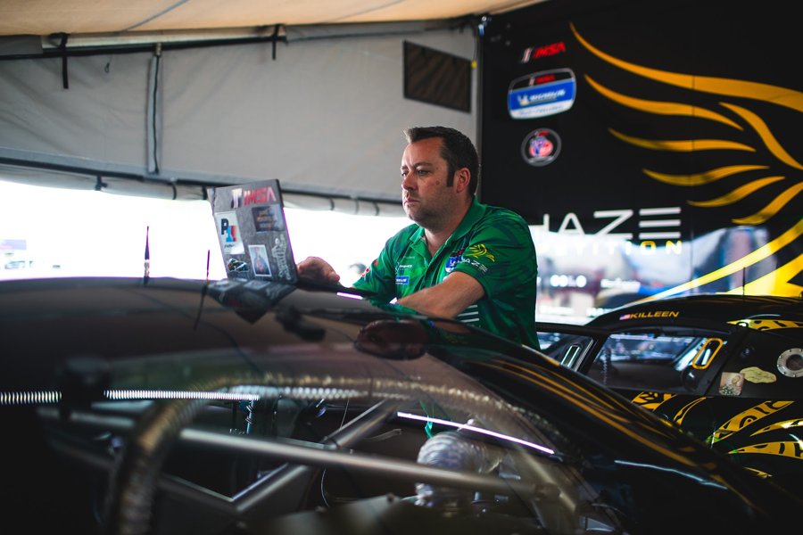 Engineer working on a laptop over the rear deck of a race car in the paddock tent