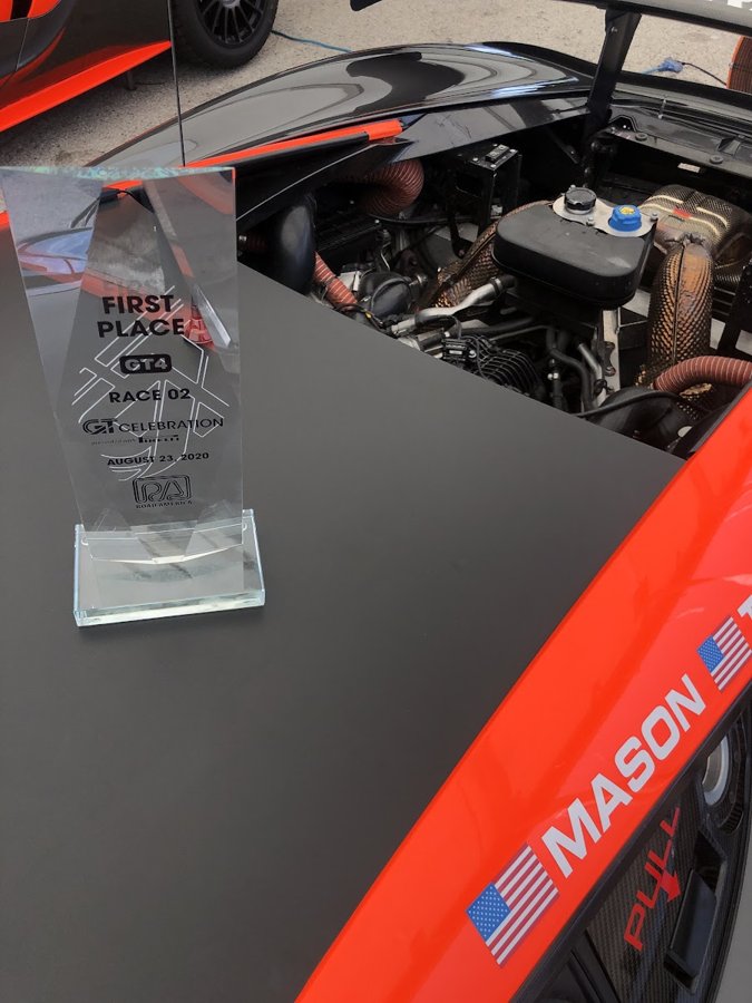 First place GT4 trophy standing on the bodywork of a race car with the engine bay open