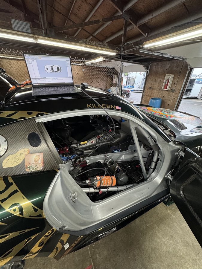 McLaren GT4 in the shop with rear bodywork removed and a laptop resting on the roof