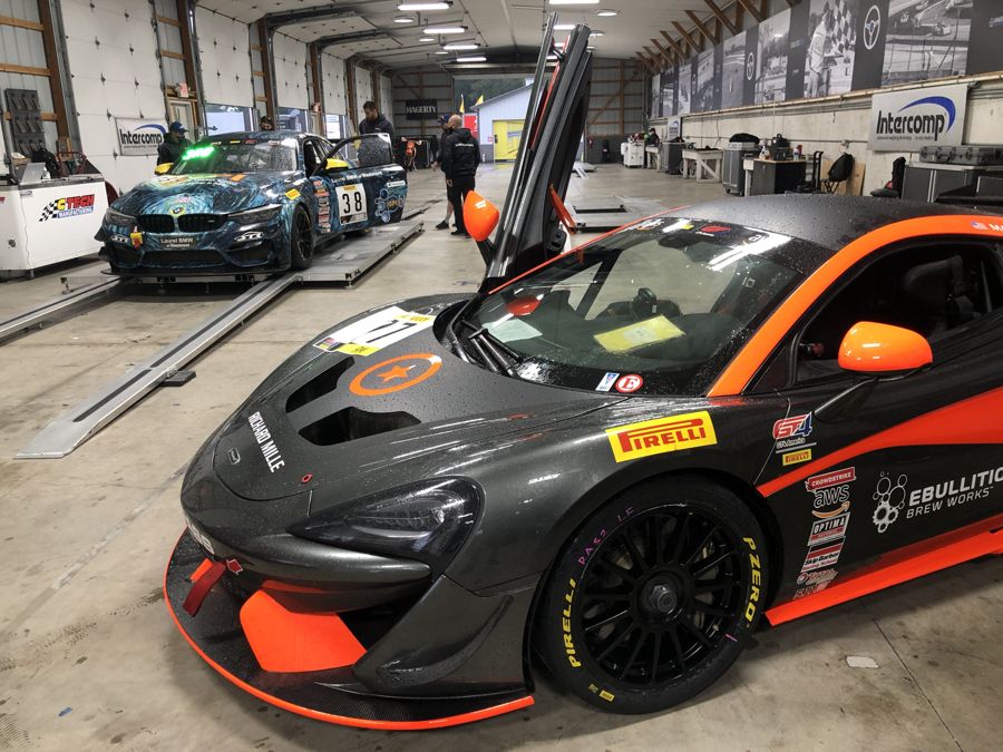 McLaren 570S GT4 on setup scales in the garage with a BMW M4 GT4 behind