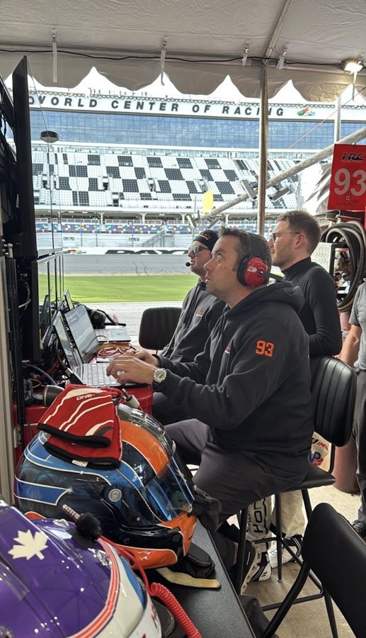 Crew with headsets watching monitors on the timing stand at Daytona with helmets staged in the foreground