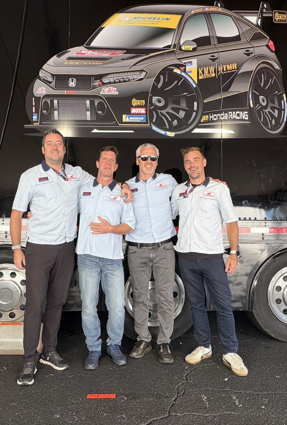 Four team members in Honda crew shirts in front of the race transporter
